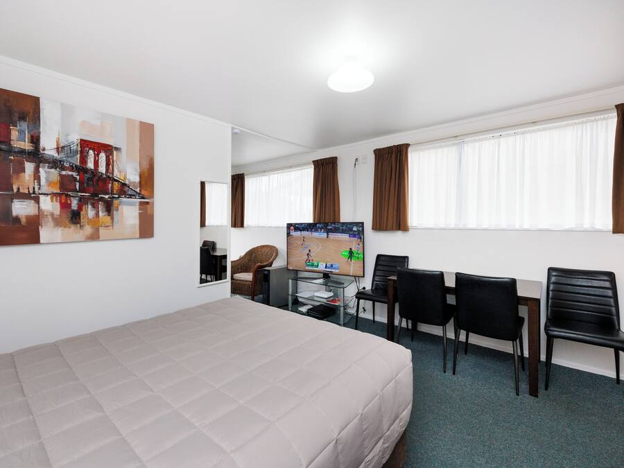 Habitación de hotel con cama, escritorio, computadora, silla y televisión.
