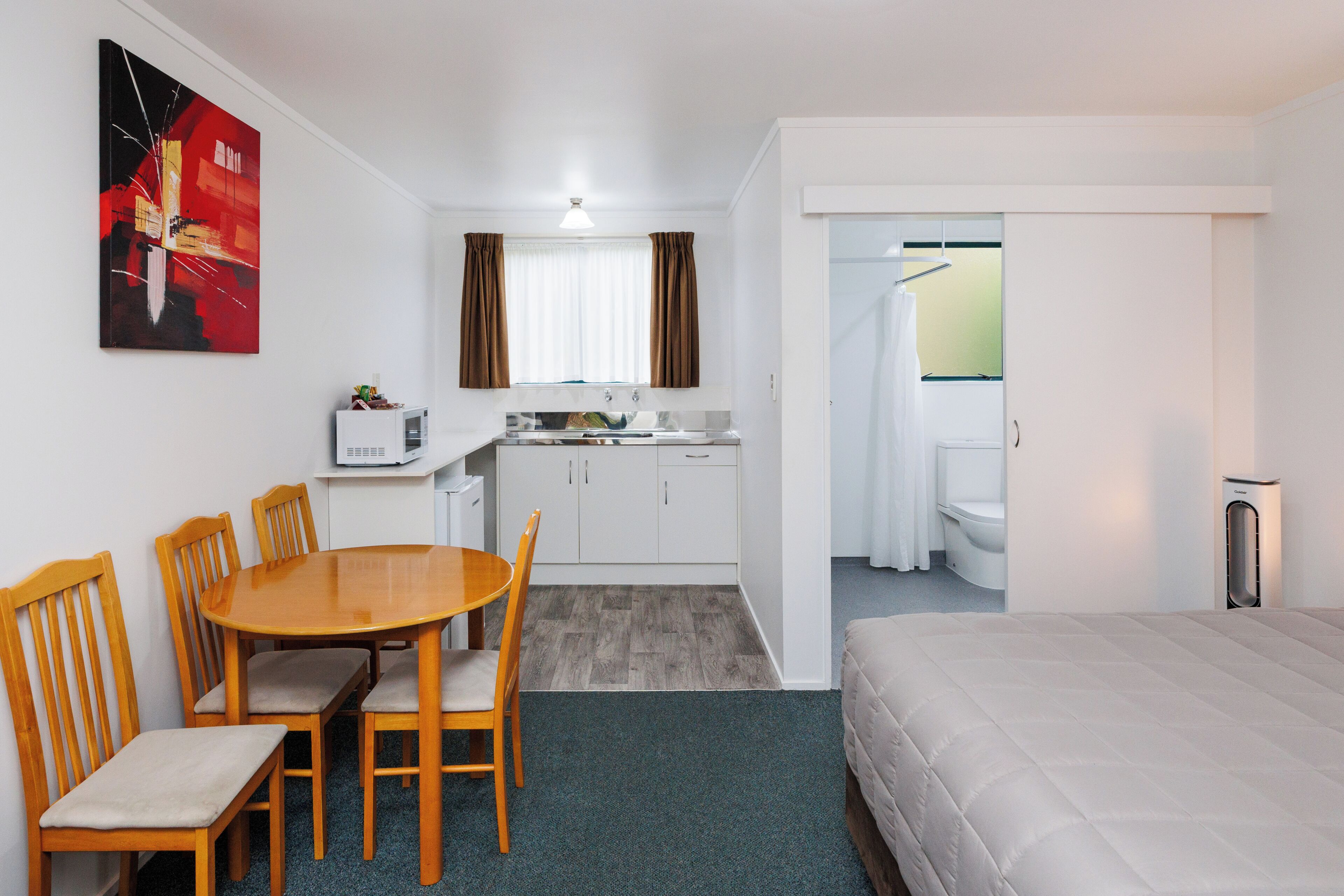 Habitación de hotel con cama, una mesa de comedor con sillas, kitchenette y zona de ducha.