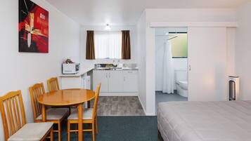 Habitación de hotel con cama, una mesa de comedor con sillas, kitchenette y zona de ducha.