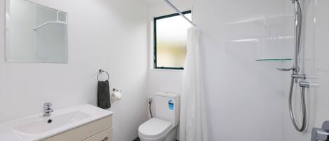 Un baño moderno con lavamanos, inodoro y ducha blancos.