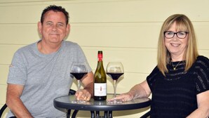 Dos personas sentadas en una mesa redonda con una botella de vino y dos copas de vino.