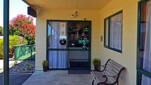 A hotel entrance with a bench, a green fence, and a potted plant.