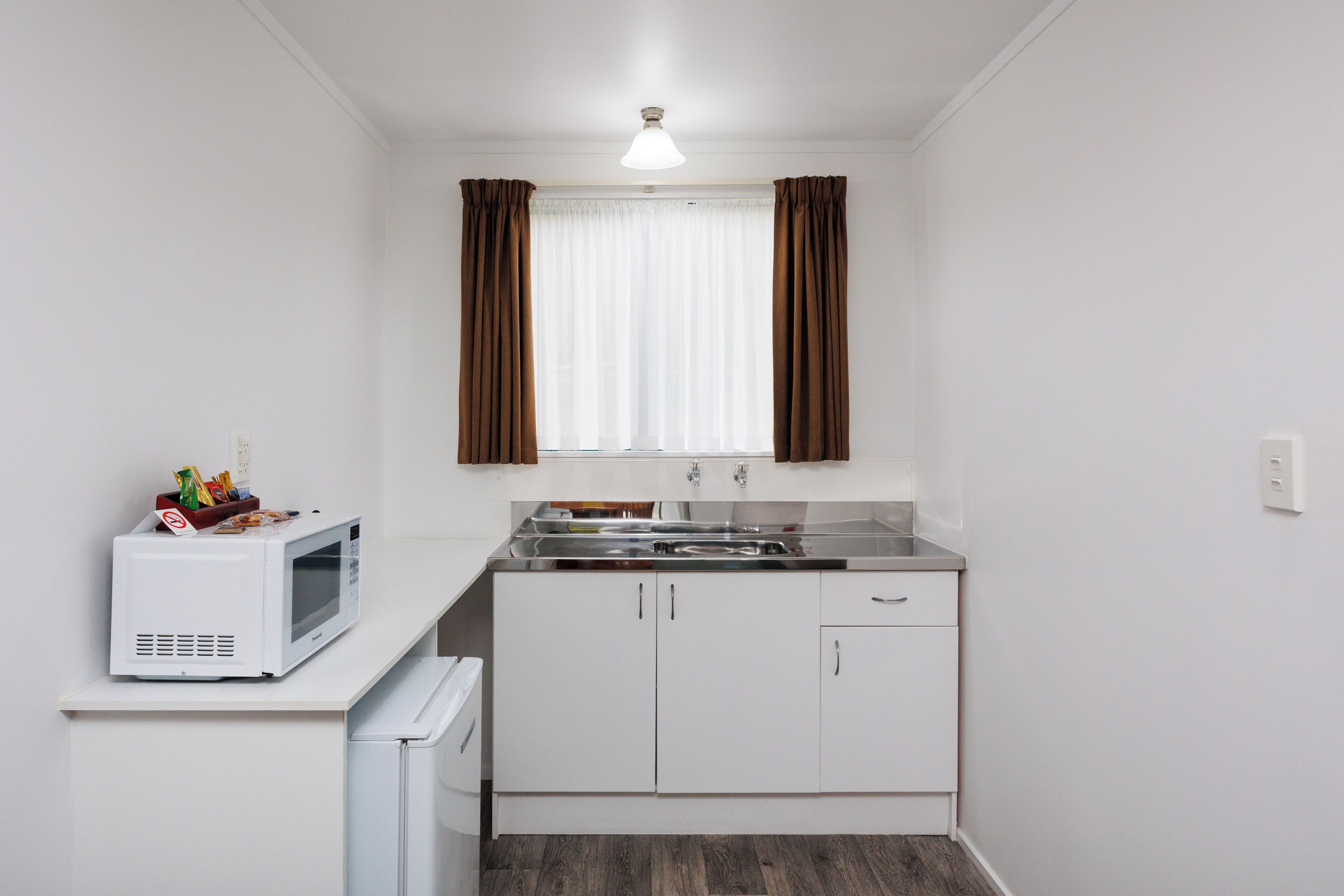 Una kitchenette compacta equipada con microondas, refrigerador, pileta y alacenas.