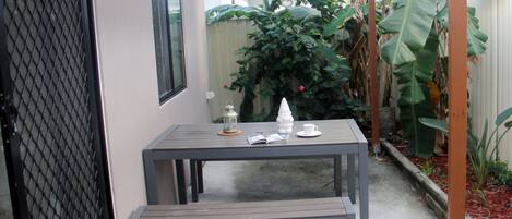 Eine Terrasse mit Tisch und Bank, umgeben von Pflanzen und einem Holzzaun.