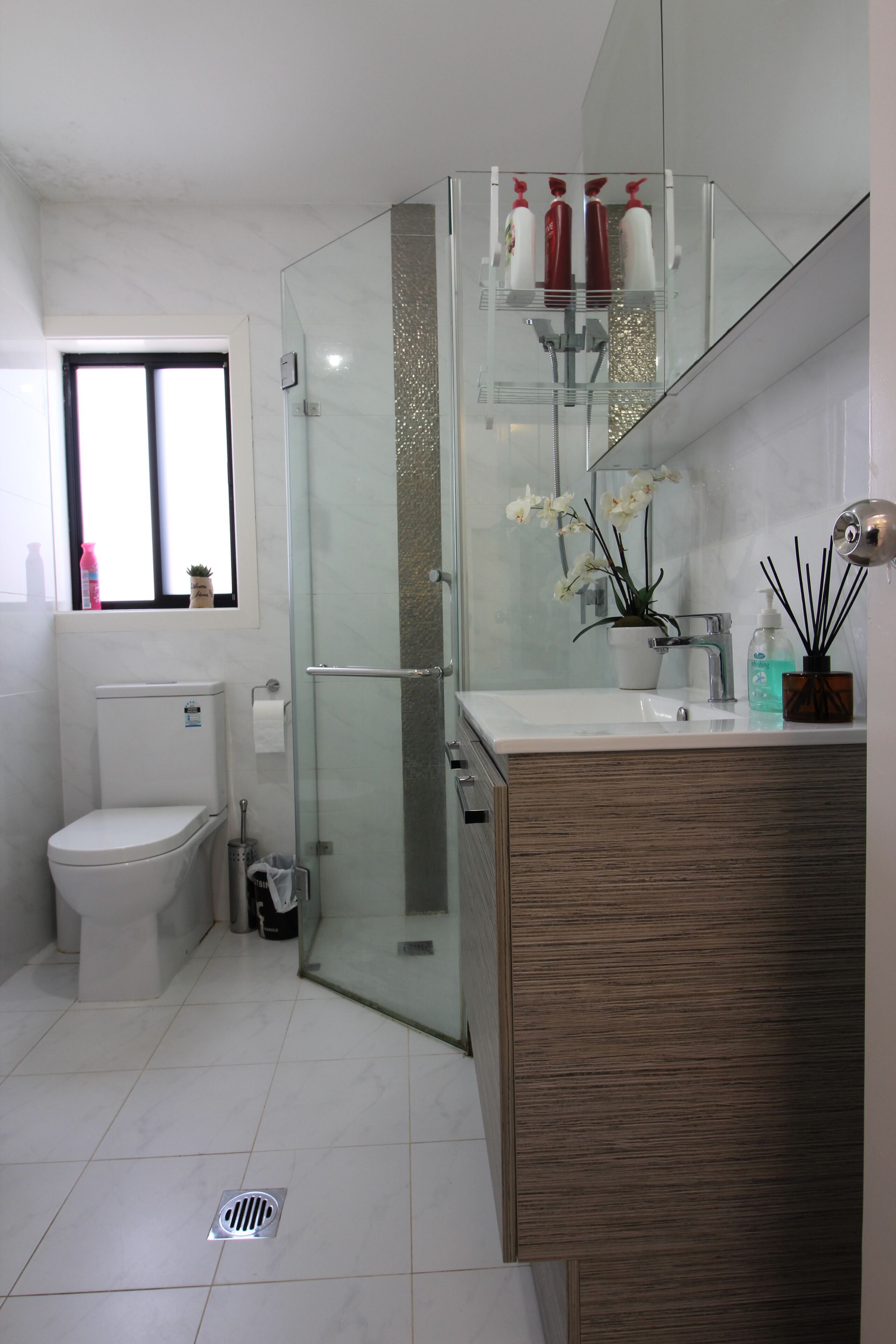 A modern bathroom with a glass shower enclosure, a white toilet, and a wooden vanity with a mirror.