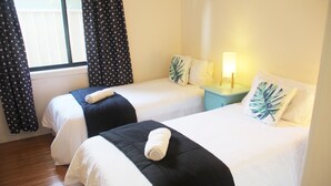 Ein Hotelzimmer mit zwei Betten, auf jedem Bett ein zusammengerolltes Handtuch. Dazwischen steht ein Nachttisch mit einer Lampe.
