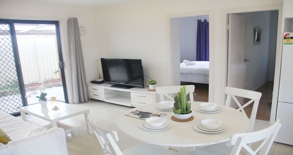 A hotel room with a dining area, a TV, a bed, and a bathroom visible through an open door.