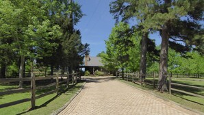A paved pathway leading to a building with a covered entrance, surrounded by trees and a wooden fence.