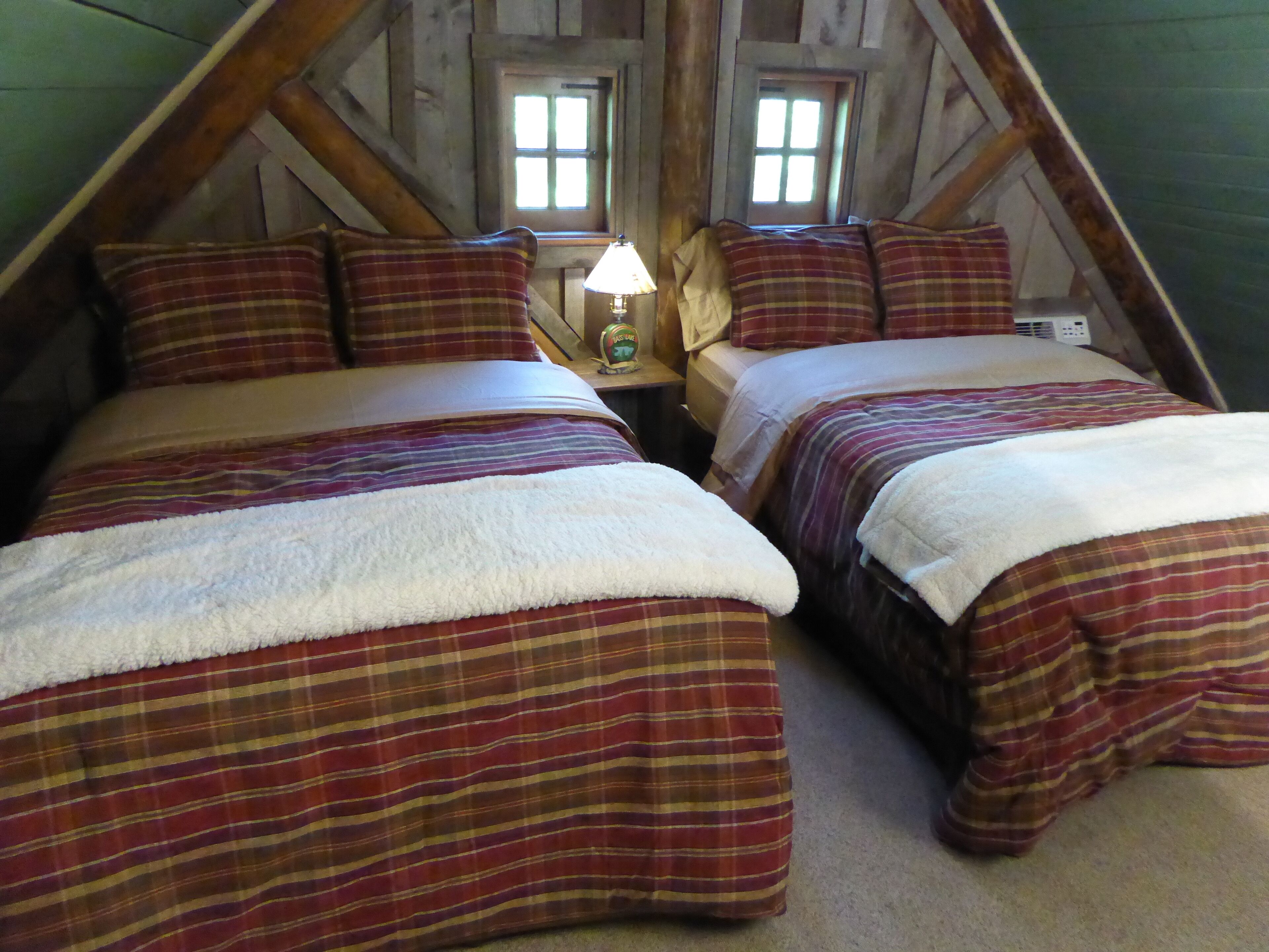 A cozy attic bedroom with two beds, plaid bedding, and a lamp on a nightstand.