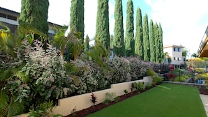 Un jardí ben cuidat amb alts cipressos, plantes en flor i un pràt impecable.