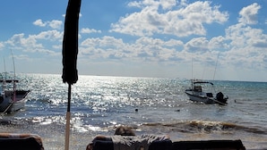 Une scène de plage avec des bateaux, un ciel dégagé et un soleil éclatant se reflétant sur l’eau.