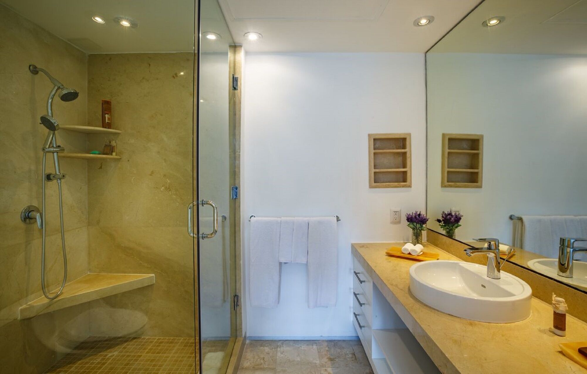 A modern bathroom with a glass shower enclosure, a large mirror, and a beige countertop with a sink and vanity.