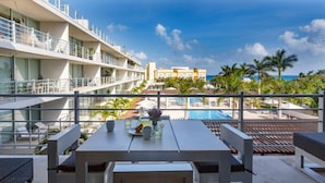 Un balcon donnant sur la piscine, un coin repas et, au loin, le bâtiment de l’hôtel.
