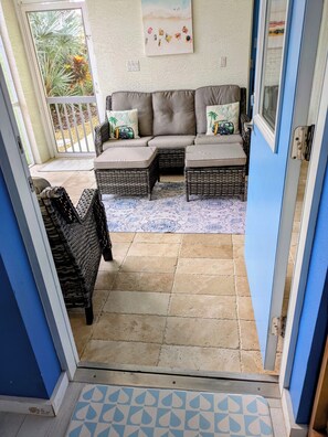 Una habitación con un conjunto de sofá, sillas de mimbre, un tapete estampado y una puerta que da al exterior.