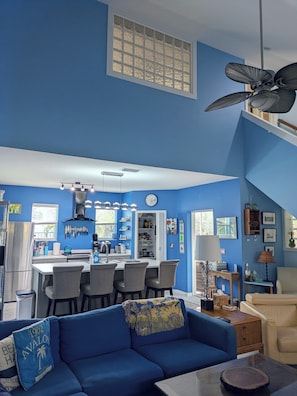Una sala de estar moderna con decoración azul, un comedor, una cocina y un ventilador de techo.