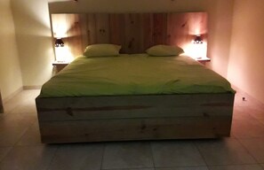 A large bed with a wooden headboard, two bedside lamps, and a tiled floor.