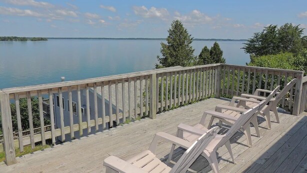 A wooden deck with chairs overlooking a calm lake, surrounded by greenery.