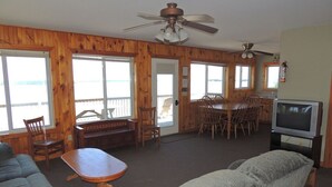 A spacious living room with a large sofa, a dining table, and chairs, wooden walls, and a television.