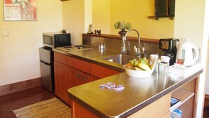 Une cuisine compacte équipée d’un évier, d’un four à micro-ondes et d’une cuisinière. Un saladier rempli de fruits est posé sur le comptoir, et il y a aussi une machine à café.