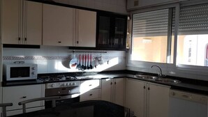 A kitchen with white cabinets, a microwave, stove, and a window with blinds.