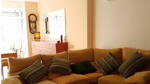 A living room with a sofa, pillows, a wooden cabinet, and a wall clock.