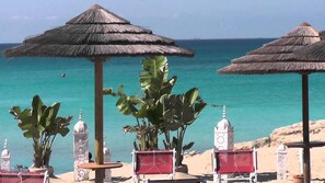 A beach with thatched umbrellas, potted plants, and a view of the ocean.