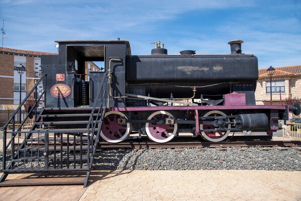Une locomotive à vapeur immobile, dotée d’un grand mécanisme circulaire à engrenages, d’une cheminée et d’un quai avec des marches menant à la cabine de la machine.