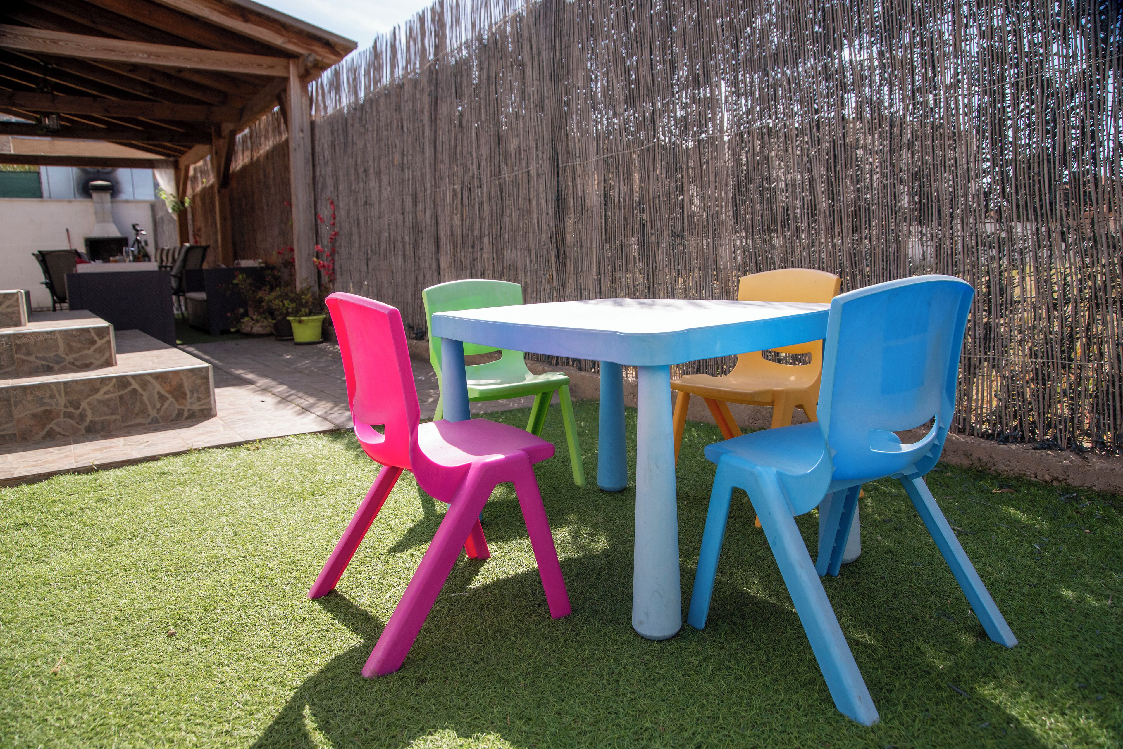 Un patio con una mesa, sillas coloridas, una valla de madera y una jardinera de piedra.