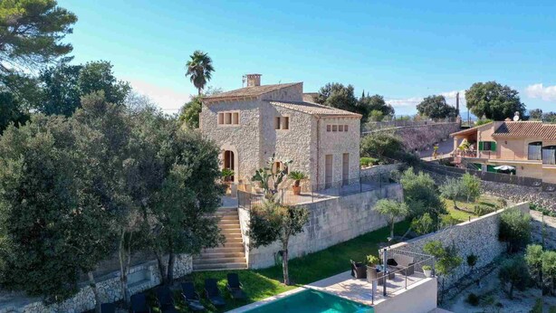 A stone villa with a swimming pool, surrounded by greenery and trees.