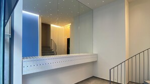 Een modern interieur met een trap, een spiegelwand en meerdere lichtarmaturen aan het plafond.