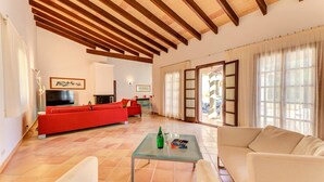 Amplia sala de estar con un sofá rojo, un sofá color beige y una mesa de centro de vidrio. Se observa un televisor y una chimenea al fondo.