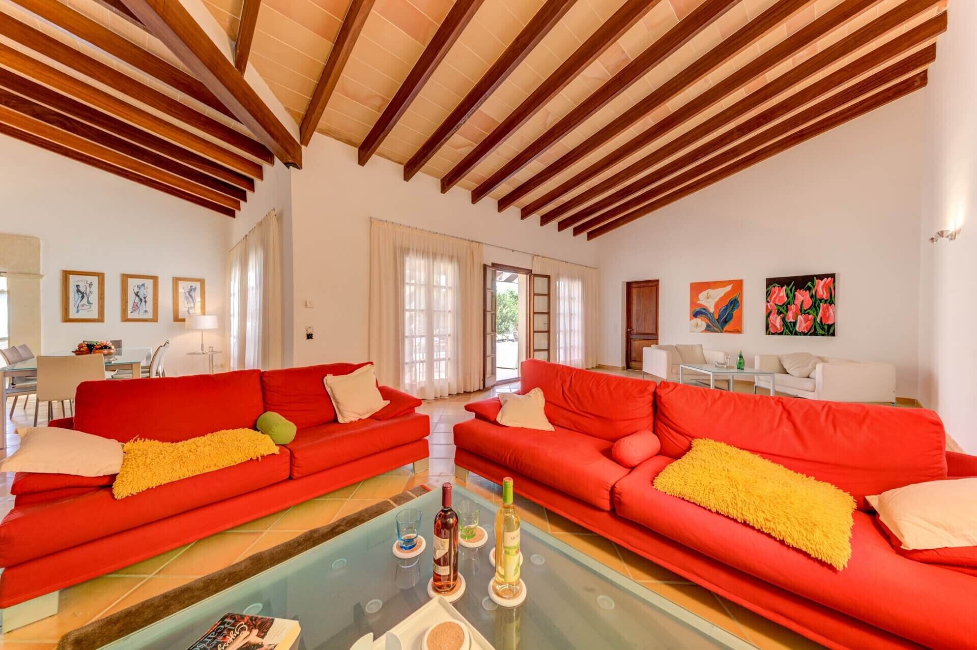 A spacious living room with two red sofas, a glass coffee table, and a dining area with a table and chairs.