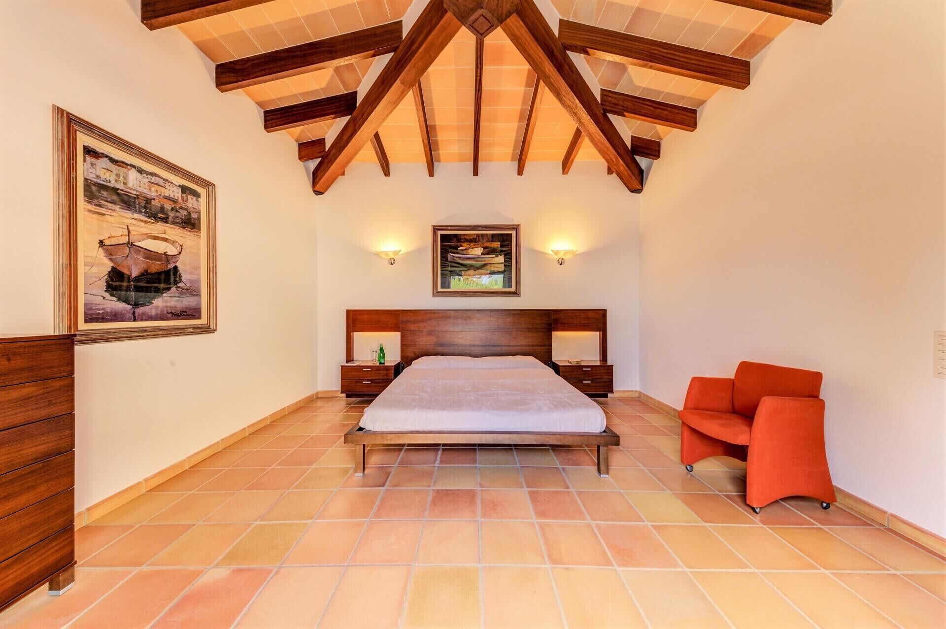 Ein Schlafzimmer mit Holzboden, einem Bett, einem Nachttisch, einem Sessel und zwei Wandleuchten.