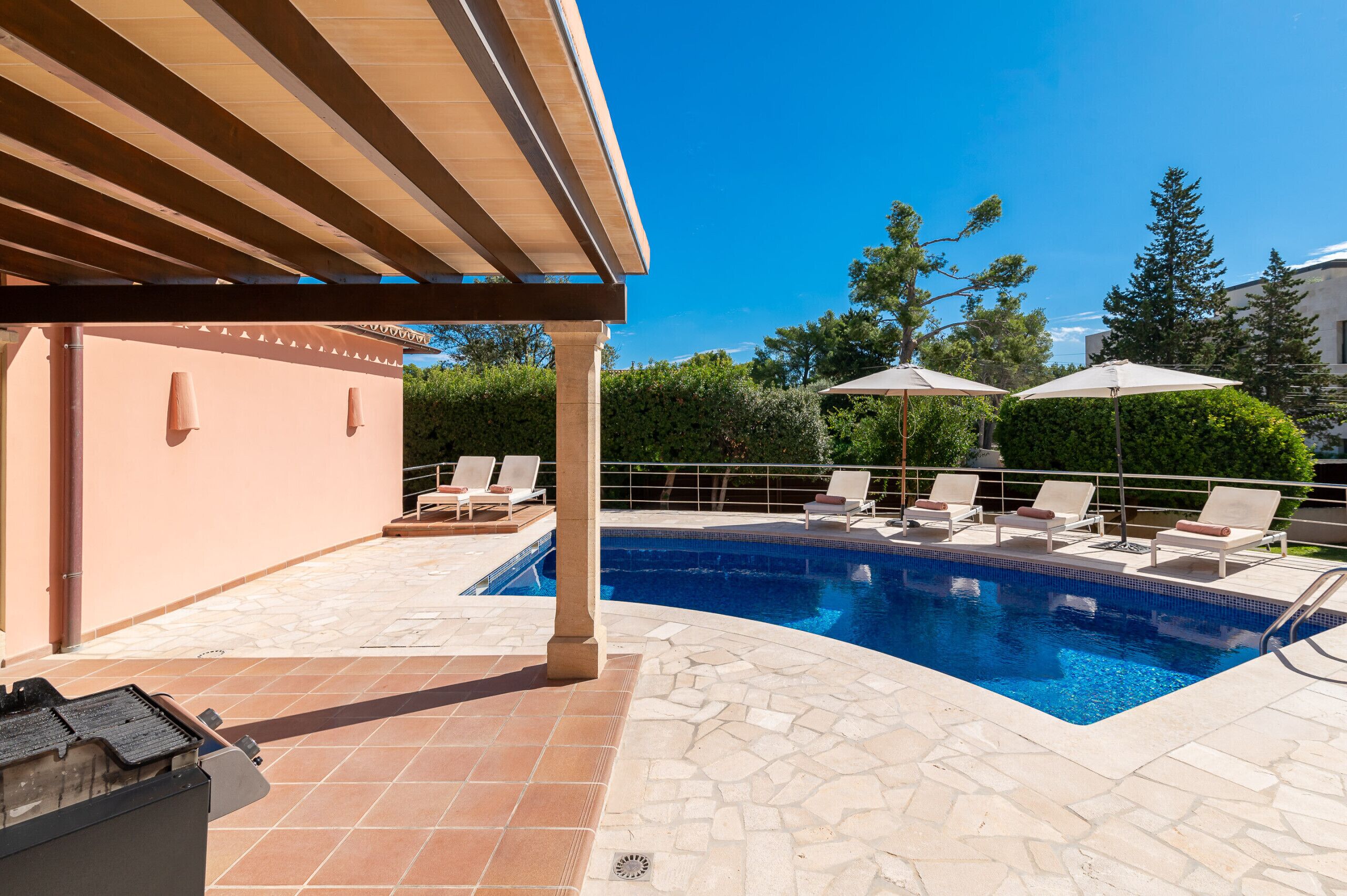 Une piscine avec des chaises longues et des parasols, une pergola et un espace barbecue.