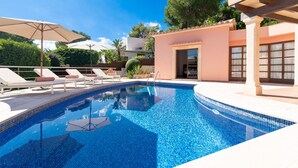 Una piscina con sillones de descanso y sombrillas, rodeada por un edificio de fachada con azulejos.