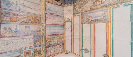 A bathroom with a large bathtub, tiled walls with historical cityscape murals, and a wooden ceiling beam.