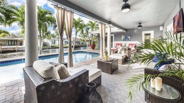 A covered outdoor area with a pool, wicker furniture, and a view of palm trees. - Spacious WATERFRONT villa, heated salt water pool, very central, beach 5 min (Oakland Park)