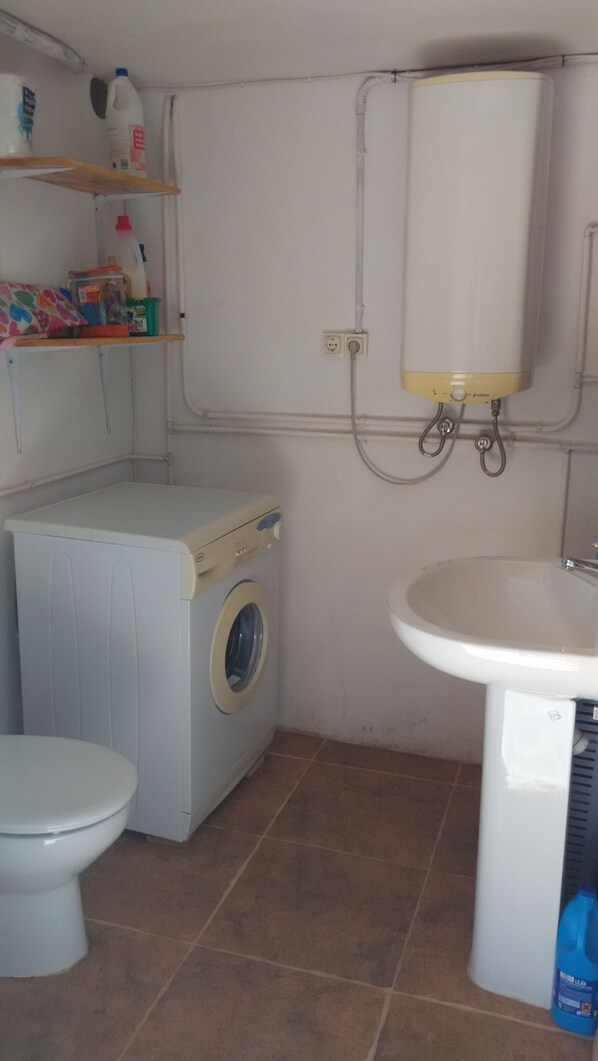 A compact bathroom with a washing machine, toilet, and sink.