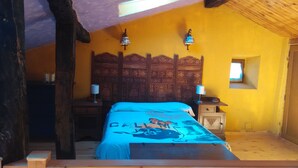 A bedroom with a wooden bed, two bedside tables with lamps, a decorative headboard, and a small window.