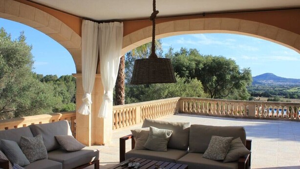 A covered outdoor seating area with two sofas and a coffee table, a hanging light fixture, and a view of the landscape. - Cottage `Es Garballó`. (Son Servera)