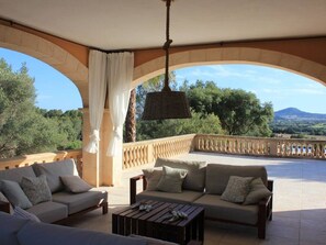 A covered outdoor seating area with two sofas and a coffee table, a hanging light fixture, and a view of the landscape. - Cottage `Es Garballó`. (Son Servera)
