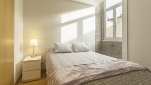 Une chambre à coucher avec un lit, une table de chevet, une lampe et une fenêtre.