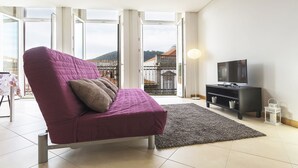 Un salon moderne avec un canapé violet, un téléviseur à écran plat et une vue sur un immeuble à travers de grandes portes vitrées.