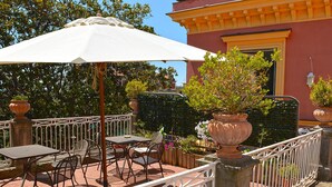Un patio exterior con mesas y sillas, rodeado por una cerca de metal blanco y macetas con plantas.