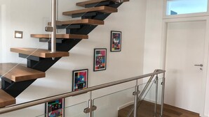 Una escalera moderna con peldaños de madera y barandillas de vidrio, que conduce a un rellano con una puerta y una ventana.