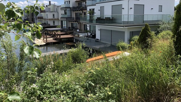 Un edificio residencial moderno con una terraza en la azotea, un área de estar al aire libre techada y vistas a un cuerpo de agua.