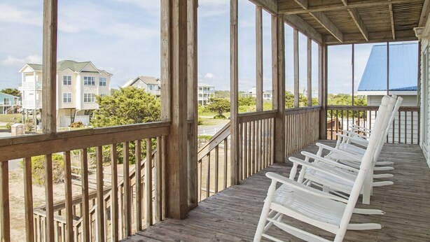 A wooden deck with white rocking chairs, overlooking a residential area with houses and greenery. - Lovely 4 Bedroom Ocean view house in West Beach (Oak Island)