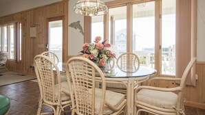 A dining area with wicker chairs, a glass table, and a floral centerpiece. - Lovely 4 Bedroom Ocean view house in West Beach (Oak Island)