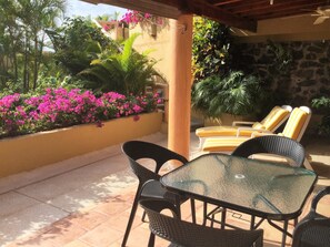 A patio with a glass table and chairs, surrounded by a yellow wall and pink flowers.