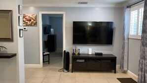 Una sala de estar con un televisor de pantalla plana montado en la pared, un mueble de entretenimiento de color oscuro y una puerta que da a otra habitación.